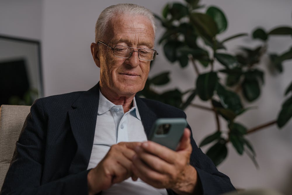 Senior man smiling while using his phone at home — daily engagement with Ramona